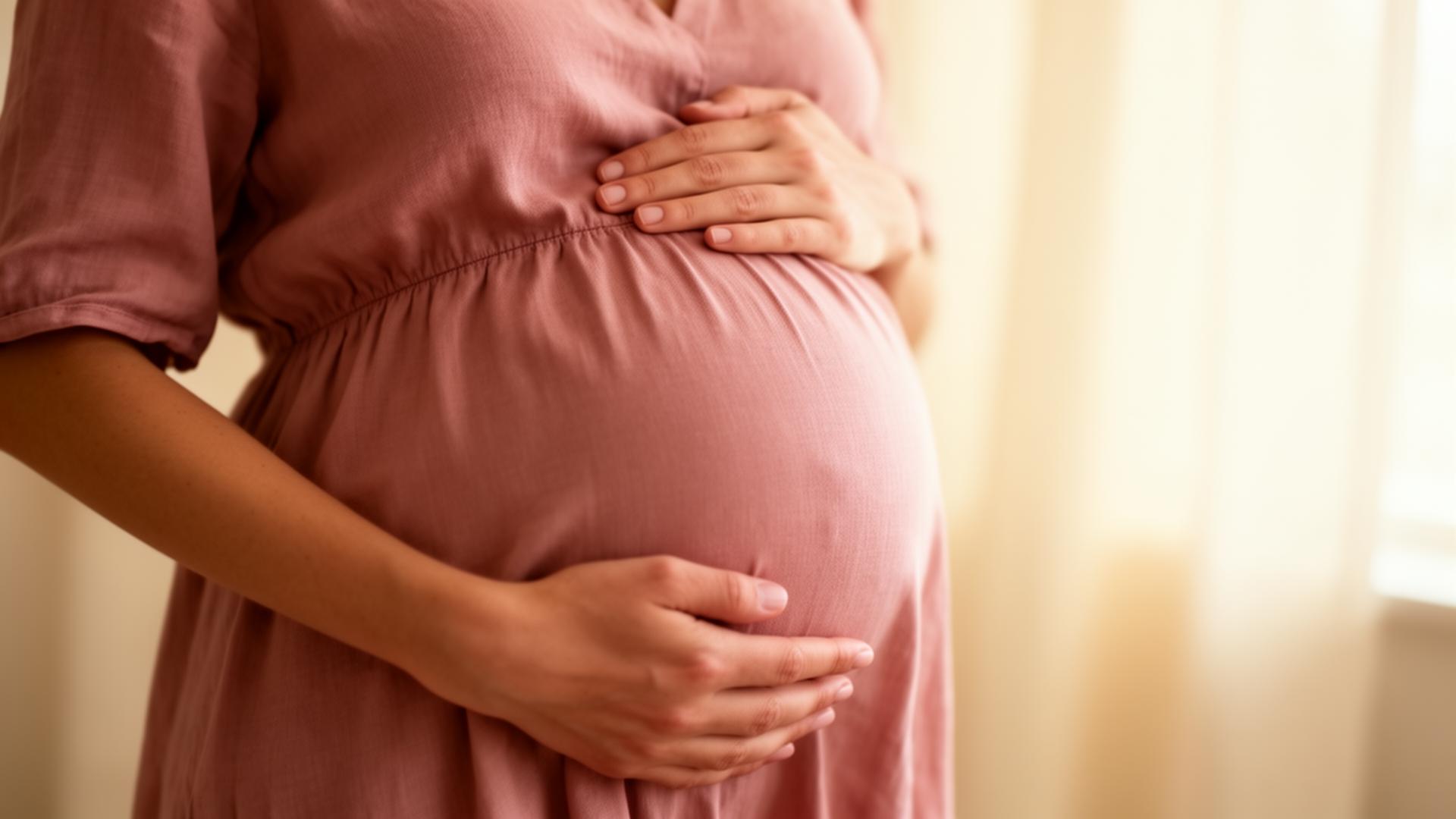 A pregnant woman cradles her belly in soft window light
