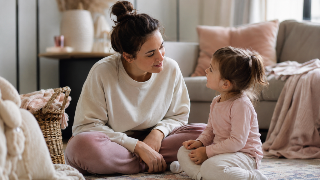 surrogacy telling your kids — warm mother sitting on the floor talking gently with her young child in a sunlit living room
